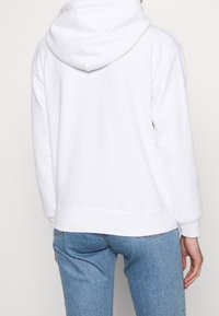 Felpa bianca con tasca a canguro, polsini e orlo a costine, realizzata in morbido tessuto misto cotone, con cappuccio aderente e vestibilità comoda.