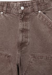 Jean en denim marron avec poches avant, passants de ceinture, fermeture par boutons et coutures visibles.