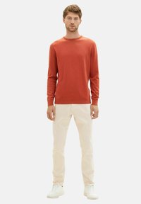 Jersey rojo de manga larga en tela suave, de cuello redondo y corte ajustado. Combinado con jeans de color claro y zapatillas blancas. Diseño simple y moderno.