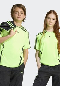Neon gule treningsskjorter med svarte detaljer, korte ermer og ledig passform, kombinert med svarte treningsbukser. Adidas-logoen vises tydelig.