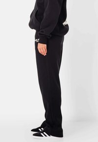 Zwarte sweatpants van zachte stof met een elastische tailleband. Heeft een relaxte pasvorm en nauwsluitende enkels. Gecombineerd met zwarte sneakers met witte strepen.