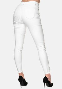 Pantalones vaqueros blancos ajustados con una cintura alta, con una textura suave, bolsillos traseros y dobladillos deshilachados, combinados con zapatos de tacón altos negros.