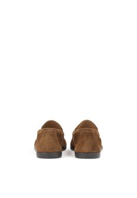 Mocassins en daim marron avec orteils arrondis, semelles noires plates et détails de couture minimaux, présentant une doublure intérieure lisse.