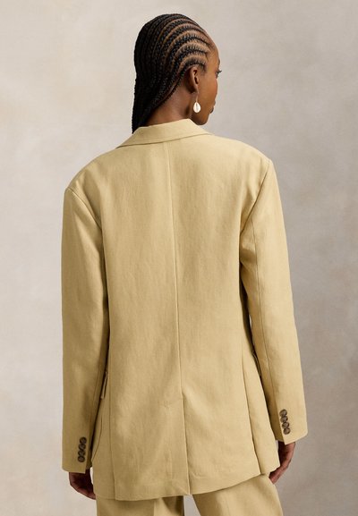 Ανοιχτό κίτρινο υπερμεγέθες σακάκι με δομημένους ώμους, δύο πλαϊνές τσέπες και μανσέτες με κουμπιά. Κατασκευασμένο από υφασμάτινη ύλη με υφή και λείο φινίρισμα.