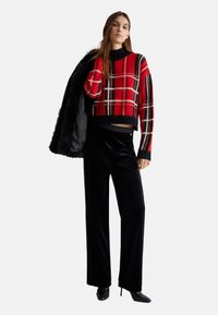 Rød og sort ternet cropped sweater med høj hals, parret med sorte velour wide-leg bukser og spidse sorte hæle.