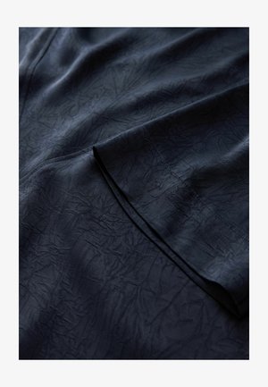 Temno modri tkanina z gubanjem, ki ima gladko površino in rahlo sijaj. Robovi so čisto zašiti in prikazujejo rahlo sijajno površino.