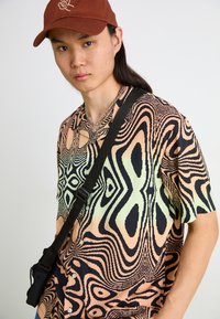 Chemise à manches courtes avec un motif abstrait multicolore dans des teintes de noir, pêche et menthe ; doté de boutons et d'une coupe décontractée.