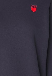 Sudadera azul marino con texto bordado en rojo que dice "LOVE" y un icono de corazón. Textura suave con un diseño clásico de cuello redondo.