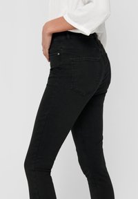 Jeans de mezclilla negra con un corte ajustado, cintura a media altura, diseño de cinco bolsillos y detalles de costura sutiles. Tejido texturizado con ligero estiramiento.