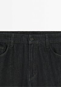 Taille de jean en denim noir avec fermeture par bouton, passants de ceinture et poches avant visibles sur fond blanc.