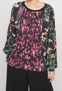 Schwarze Bluse mit floralem Muster in Pink, Weiß und Grün. Verfügt über ein plissiertes Design und lange Ärmel mit elastischen Bündchen. Rundhalsausschnitt.