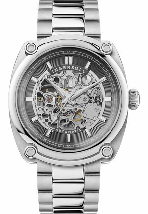 Montre automatique en argent avec un cadran squelette, mettant en valeur des engrenages et des mécanismes complexes. Dotée d'un bracelet en acier inoxydable et d'un boîtier rond.