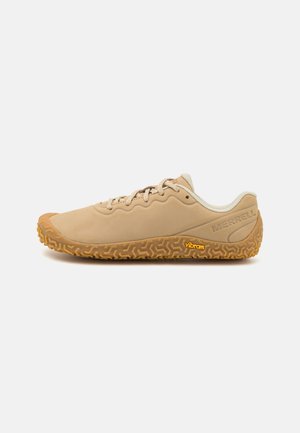 Zapato beige claro con un upper liso, suela de goma texturizada y logo naranja de Vibram; cuenta con cordones planos y un diseño de perfil bajo.