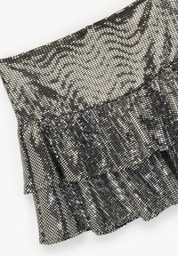 Czarna i srebrna tkanina cekinowa z plisowanym detalem falbany. Powierzchnia ma teksturę z siatką błyszczących kwadratów.