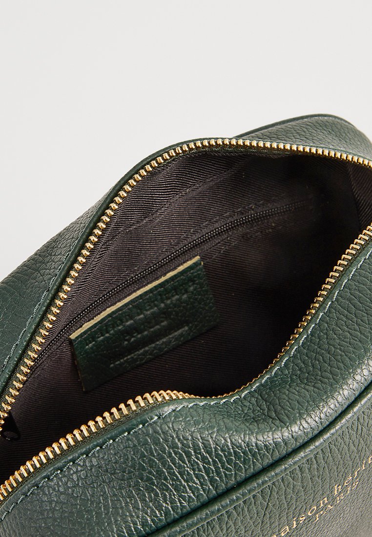 Pochette en cuir texturé vert avec une fermeture éclair dorée. Intérieur doublé de tissu noir, avec une poche zippée et une petite étiquette à l'intérieur.