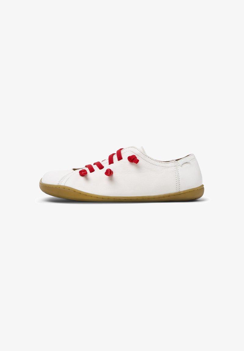 White leather shoe with red fabric laces, low profile, rounded toe, and a flexible tan rubber sole. Minimalist design with no visible branding.