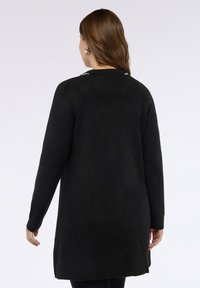 Schwarzer langärmeliger Cardigan aus weichem Stoff, mit strukturierter Oberfläche und Seitenschlitzen für Bewegungsfreiheit. Schlichtes Design, kein Muster.