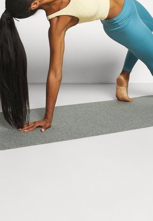 Yoga houding op een grijze mat; gekleed in een aansluitend lichtgele top en blauwe leggings, die een gestructureerde stof en een slank ontwerp tonen.