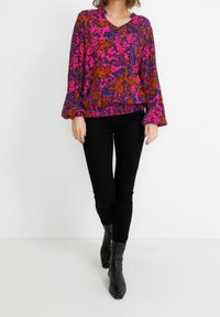 Mönstrad blus med flerfärgade blommor, V-ringning och trumpetärmar, kombinerad med svarta skinny jeans och svarta ankelstövlar.