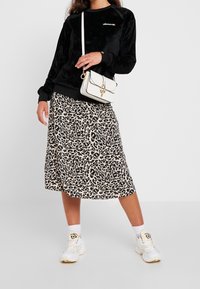 Sweat-shirt en velours noir, jupe midi imprimé léopard, sac à bandoulière blanc, et baskets blanches avec un branding discret. Textures lisses et design en couches.