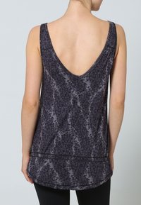 Mörkgrå ärmlös topp med V-ringning och geometriskt mönster, tillverkad av lätt tyg, med en rundad nederkant och kontrasterande sömmar.