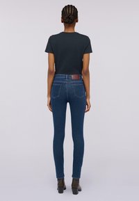 Mörk t-shirt i kombination med tajta mörkblå jeans med en lätt blekning, bakfickor och en läderlapp vid midjan. Svarta ankelstövlar.