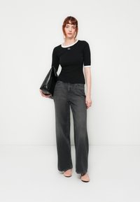 Black short-sleeve top with white trim, paired with loose, dark gray jeans and light pink heels. Holds a black oversized handbag.