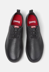 Scarpe nere in pelle con superficie strutturata, punta rotonda e design con lacci. Soletti rossi con marchio "CAMPER". Suola nera semplice.