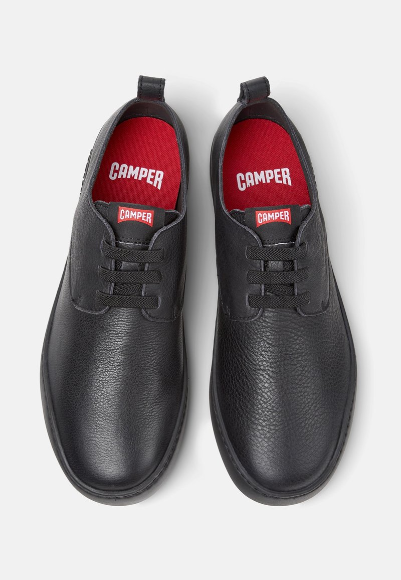 Schwarze Lederschuhe mit strukturierter Oberfläche, rundem Zehenbereich und Schnürdesign. Rote Innensohlen mit "CAMPER"-Markenaufdruck. Schlichte schwarze Sohle.