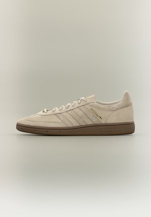 Béžové tenisky Adidas Spezial s texturovanými pruhy, zlatým logem, předním zavazováním na tkaničky a hnědou gumovou podrážkou na neutrálním pozadí.