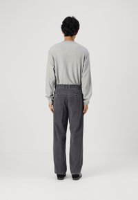 Grijze langwerpige shirt met ribbelstructuur, gecombineerd met donkergrijze corduroy broek met een rechte pasvorm en achterzakken, gezien van achteren.