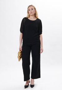 Maglia nera a maglia larga con maniche corte, abbinata a pantaloni neri a gamba larga. Accessoriata con una pochette metallica dorata e scarpe nere con punta affilata.