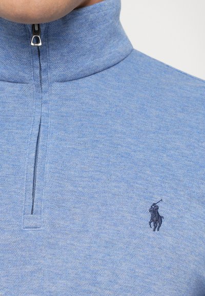 Sweater em azul claro com meia abertura e colarinho alto, com o logótipo bordado de jogador de polo em azul escuro no peito.