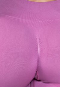 Detailní záběr na osobu, která má na sobě těsně padnoucí texturované fialové legíny, zdůrazňující detaily látky a kontury.