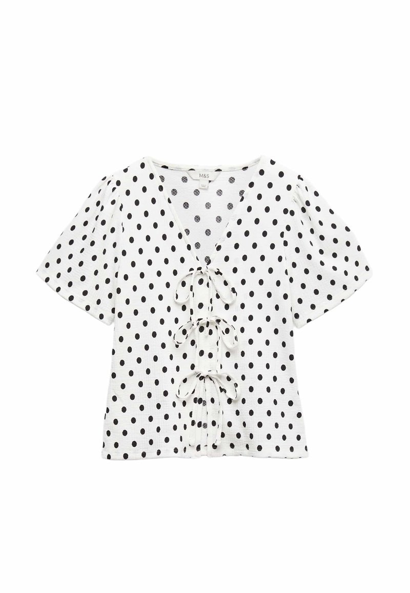 Hvid top med sorte polkaprikker, dyb V-udskæring og korte puffede ærmer. Har tre bindebånd fremme. Blød tekstur.