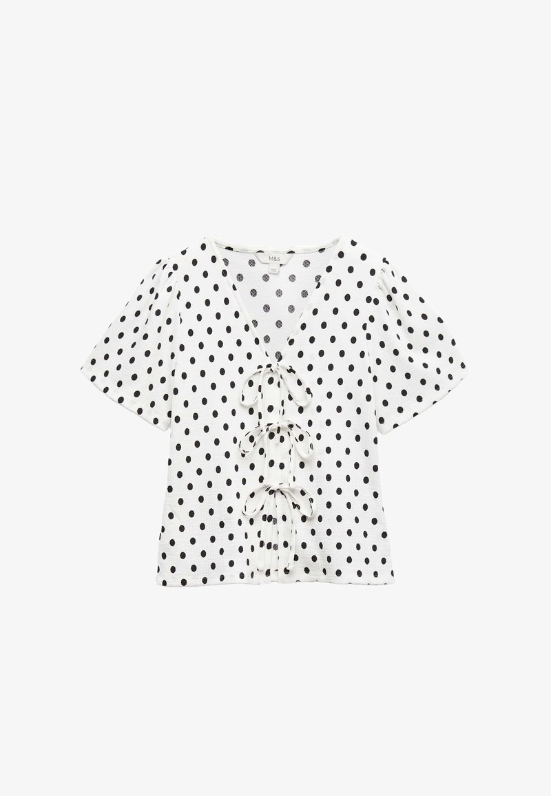 Hvid top med sorte polkaprikker, dyb V-udskæring og korte puffede ærmer. Har tre bindebånd fremme. Blød tekstur.