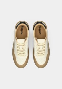 White leather sneakers with tan accents, featuring a perforated toe, round laces, and a textured gum rubber sole. Brand name visible inside.