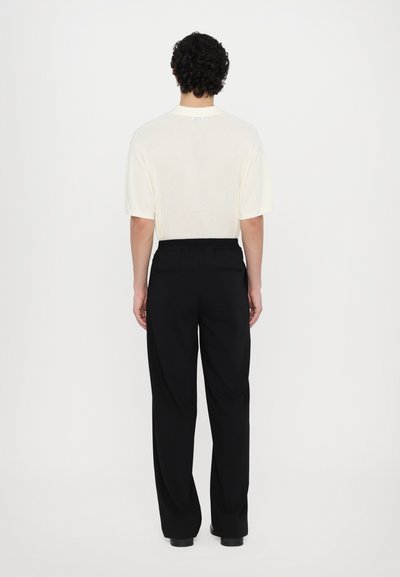Light beige knit short-sleeve shirt with a round neckline, paired with black tailored trousers featuring a relaxed fit and elastic waistband.