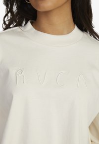 Cream-colored cotton sweatshirt featuring a round neckline and embroidered "RVCA" logo in white thread on the front. Soft texture.