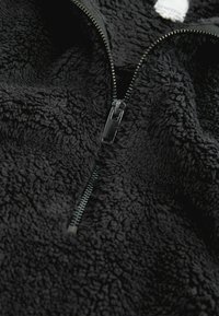 Zwarte fleece pullover met een ritssluiting aan de voorkant. Zacht, gestructureerd materiaal met een pluizige oppervlakte. De rits heeft metallic accenten.
