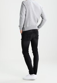 Sudadera gris con puños acanalados, combinada con jeans pitillo negros con detalles desgastados y zapatillas blancas. Fondo neutral.