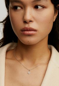 Collar de plata con un colgante de iniciales dobles, cadena delicada, diseño elegante y textura pulida, llevado sobre un fondo neutro.