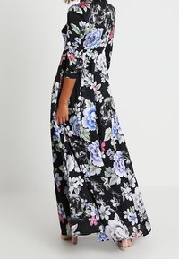 Robe maxi noire à fleurs avec des motifs floraux blancs, bleus et roses. Manches longues et tissu fluide mettant en valeur le motif vibrant et détaillé.