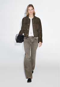 Giacca in suede marrone, t-shirt chiara e jeans grigi a zampa d'elefante. Borsa nera e scarpe nere eleganti. Design semplice, palette di colori neutri.