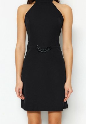 Black halter dress with a fitted bodice, a waist accentuated by a black chain belt, and a flared skirt. Smooth texture, knee-length hem.