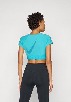 Turquoise cropped athletic top with short sleeves, featuring a diagonal black Nike logo and a textured hem, paired with high-waisted black leggings.