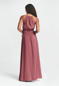 Maxi suknelė gilių rožių spalvos, pagaminta iš lygaus audinio, su halterio kaklu, susirinkusia juosmens dalimi su raišteliu ir plačiu sijonu.