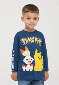 Granatowa koszulka z długim rękawem z grafiką Pokémon z przodu, zawierająca Scorbunny i Pikachu, z białym napisem "Musisz je wszystkie złapać!" na rękawie.