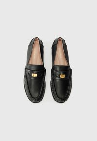 Black leather loafers with a rounded toe, gold-tone hardware, and a stitched design along the sole. Smooth texture and minimal detailing.
