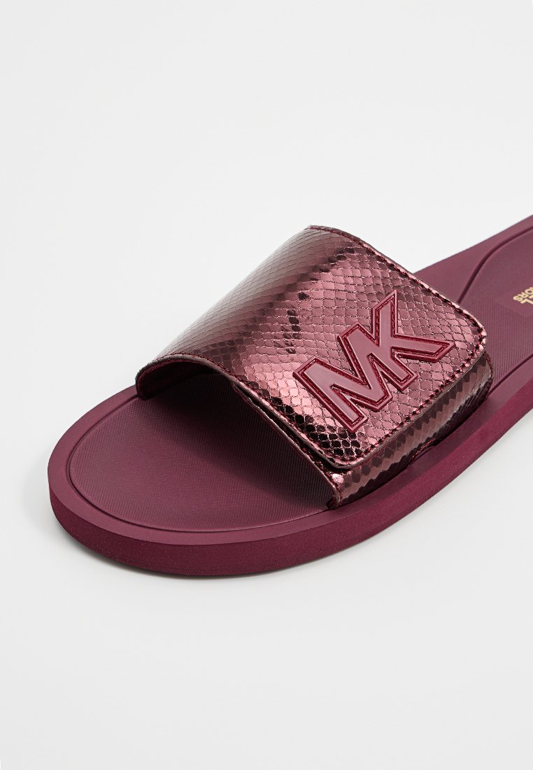 Magenta klapki z teksturowanym, metalicznym paskiem w wzór węża i gumową podeszwą. Posiada wytłoczone logo "MK" na pasku.